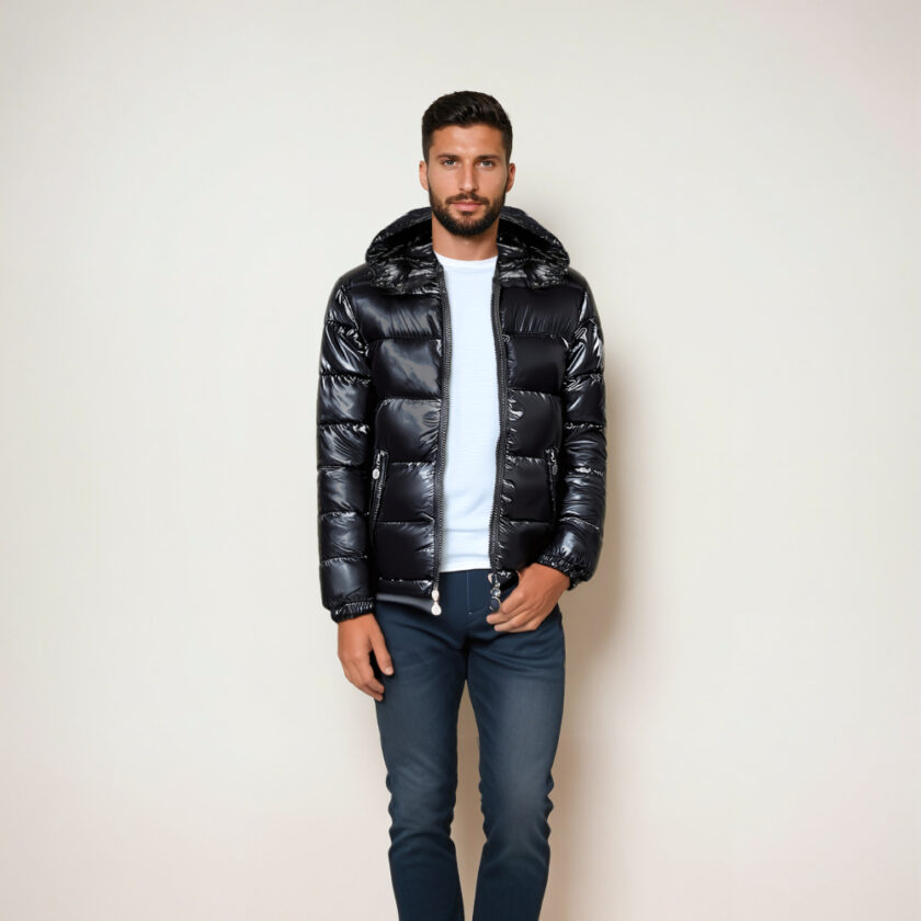 Homme brun mal rasé portant un jean bleu, un t_shirt blanc et une doudoune brillante matelassée noire à capuche. Il est devant un mur beige.