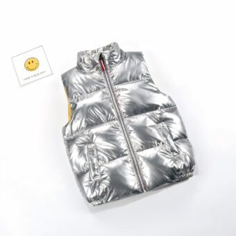 Photo d'une doudoune argentée sans manches pour enfant avec une carte smiley à côté.