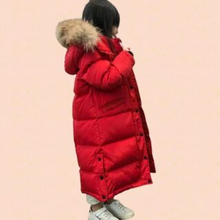 Petite fille portant une doudoune à capuche pour enfant rouge sur fond rose.