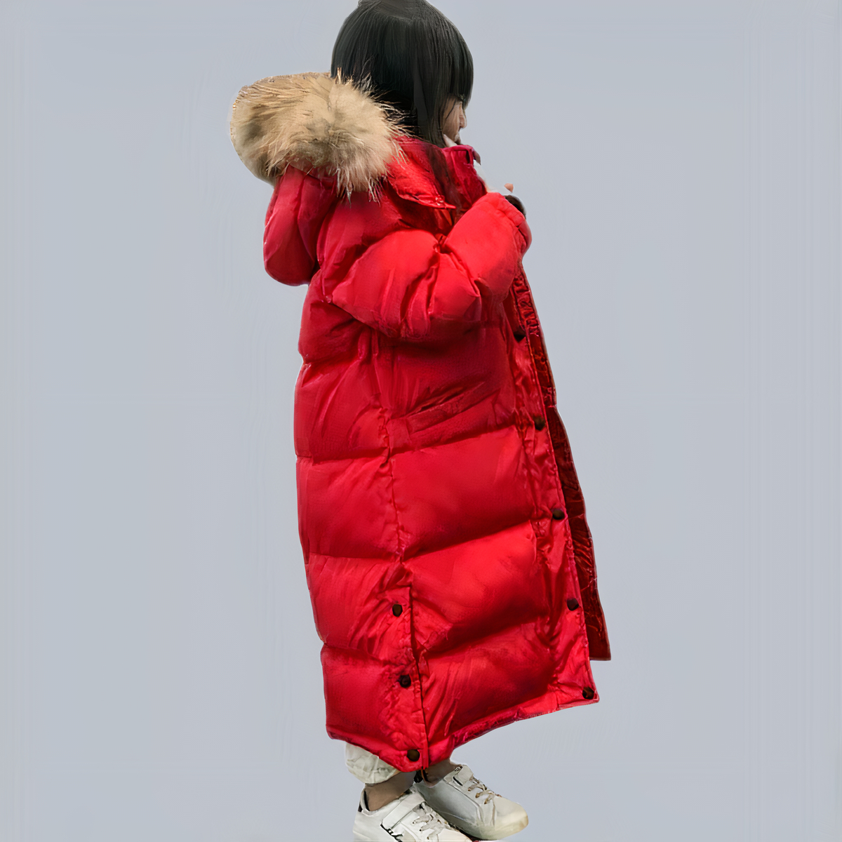 Petite fille portant une doudoune à capuche pour enfant rouge devant un fond gris.