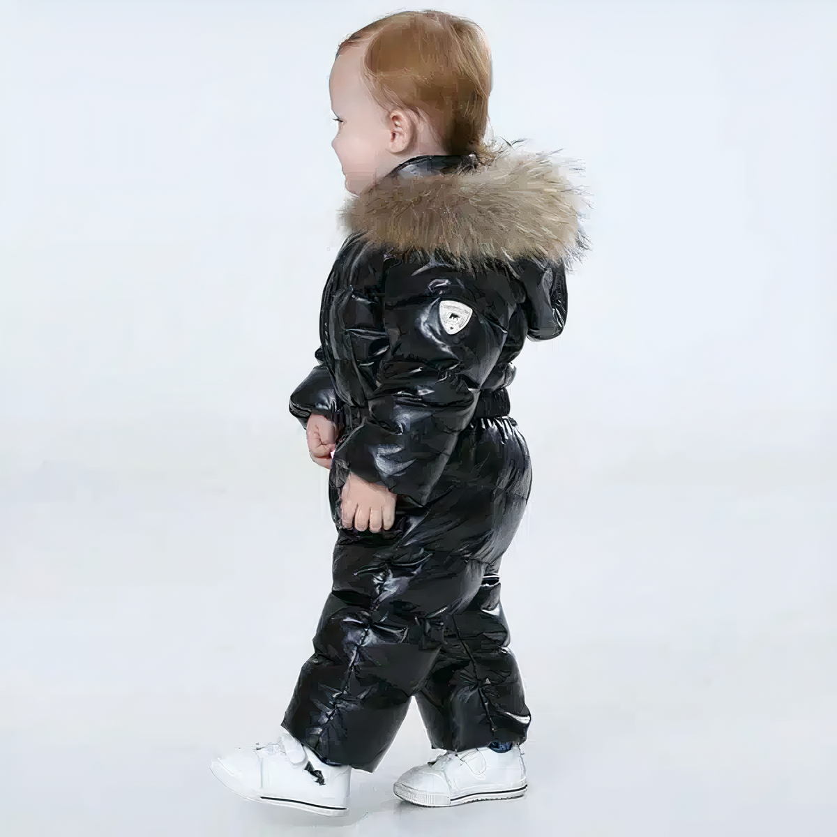 Doudoune combinaison noire pour bébé garçon porté par un petit garçon qui marche devant un fond bleu.