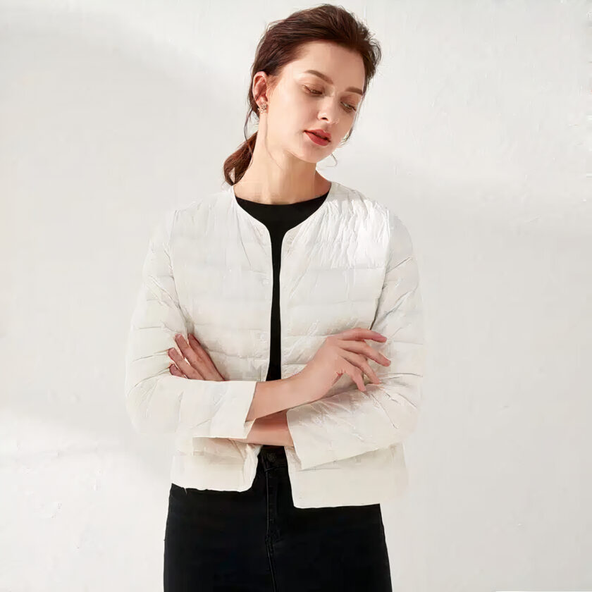 Femme portant une doudoune blanche et croisant les bras, fond blanc.