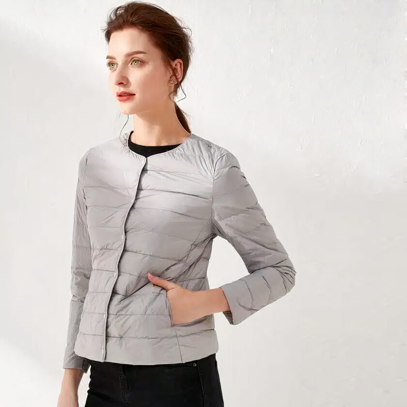 Femme portant une doudoune grise fine et un pantalon noir, fond blanc.