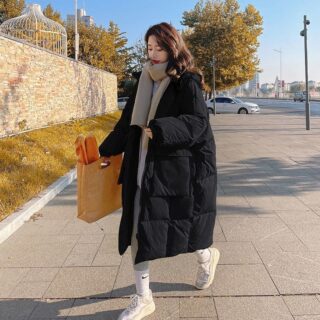 Femme portant une doudoune noire longue et tenant un sac à la main. Elle marche dans la rue.
