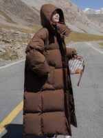 Photo d'une femme portant une doudoune à capuche longue de couleur marron sur un fond montagneux