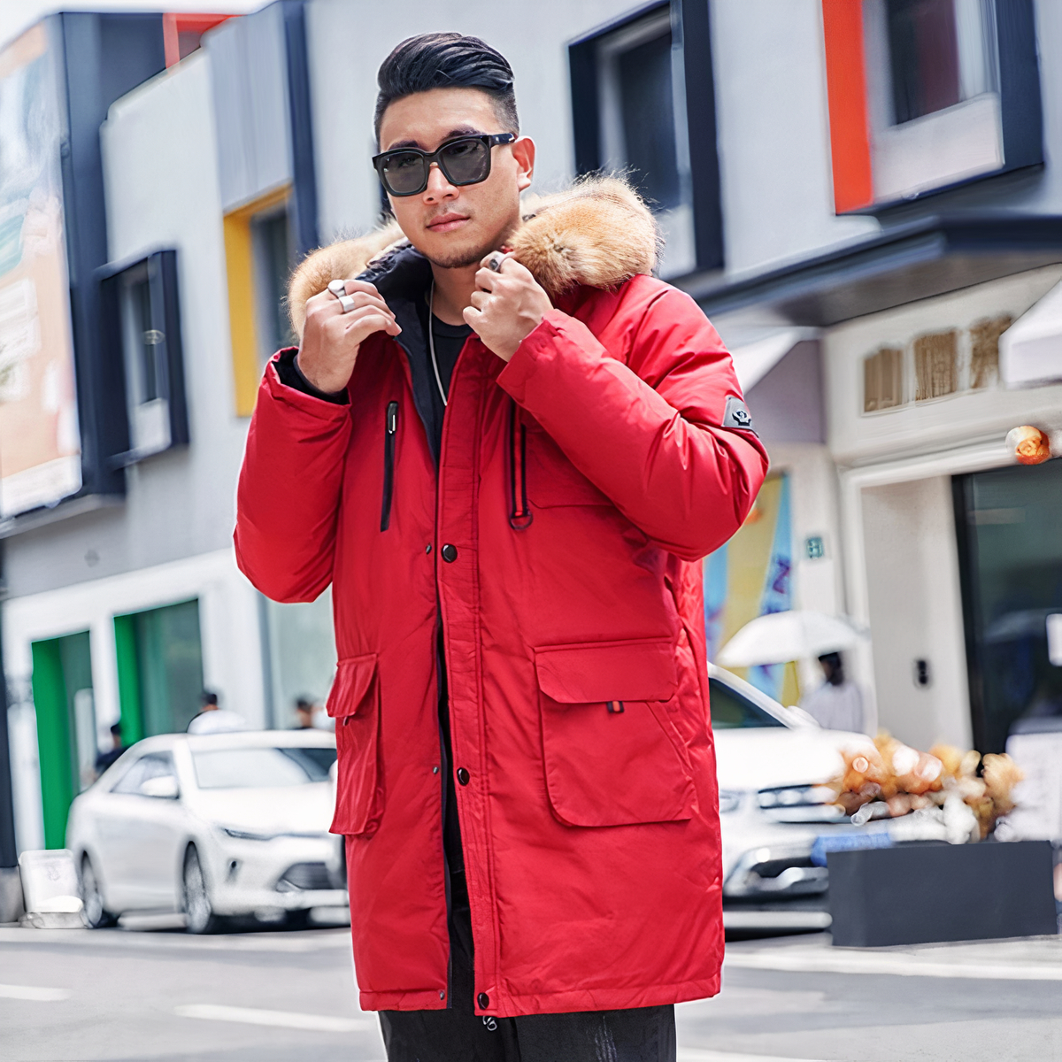 Homme portant une doudoune rouge avec capuche à fourrure, il est dans la rue.
