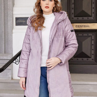 Doudoune violette ouverte avec fourrure courte sur le devant et matelassée sur les manches. Elle est portée par une femme aux cheveux longs et ondulés détachés qui a un pull blanc en dessous avec un jean bleu déchiré sur les genoux. Il y a des escaliers en arrière-plan avec une grande porte noire et dorée.