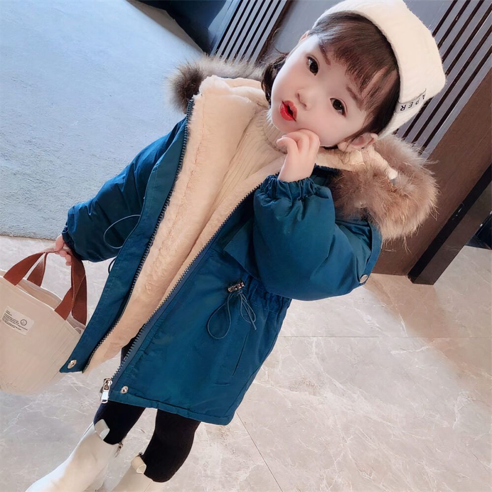 On voit une petite fille d'origine asiatique dans le hall d'un immeuble chic qui porte une doudoune bleue avec une capuche dont la bordure est agrémentée de fourrure.