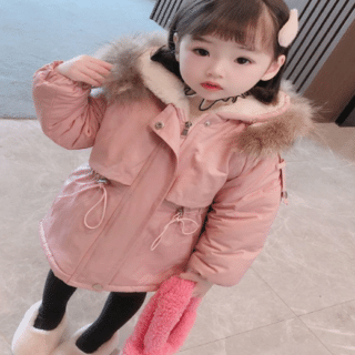 On voit une petite fille d'origine asiatique très mignonne, dans le hall d'un immeuble, qui porte une doudoune chaude rose avec une capuche doublée en polaire et fourrure.