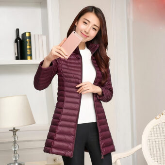 Femme portant une doudoune bordeaux et se prenant en photo avec son téléphone. On voit une lampe et une étagère derrière.