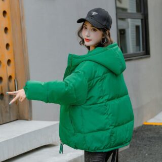Femme dans la rue portant une casquette noire et une doudoune verte à capuche.