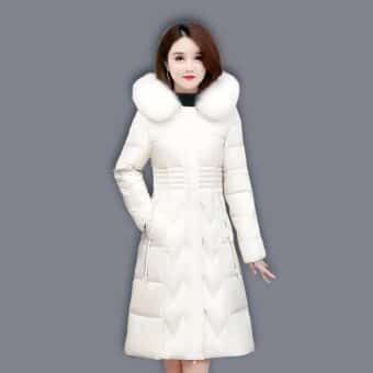 Femme asiatique brune portant une doudoune blanche longue et matelassée avec le coll en fourrure. Sa main droite dans la poche de la doudoune. Sur fond gris.