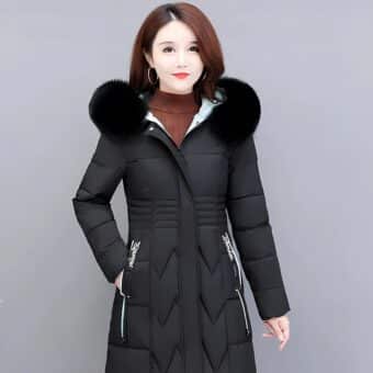 Femme asiatique aux cheveux mi_longs bruns portant une doudoune noire longue et matelassée cintrée avec de la fourrure noire sur la capuche. Elle tient sa main droite dans la poche de la doudoune. Sur fond gris.