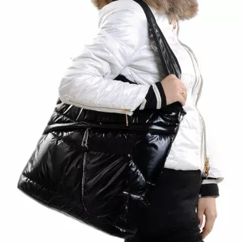 Femme de côté sans visage avec une doudoune blanche à fourrure marron qui porte un sac doudoune rectangulaire en vernis noir sur l'épaule.
