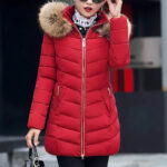 Femme brune portant des lunettes, un sac à main noire et une doudoune d'hiver mi-longue rouge dans la rue.