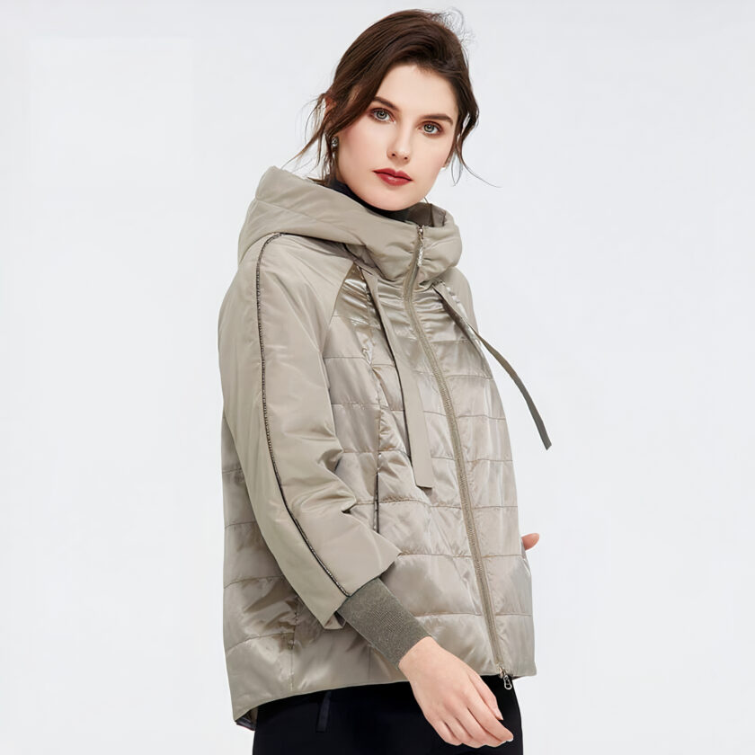 Femme brune sur fond gris portant une doudoune de printemps grande taille beige.