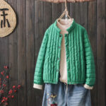 Doudoune verte type blouson porté par un cintre suspendu, par dessus un pull et un jean.