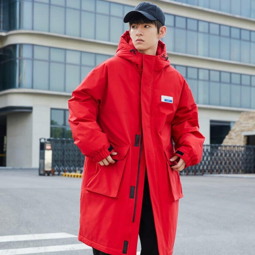 Image d'un homme portant une doudoune mi-longue rouge et une casquette bleu marine. Il est debout dans la rue avec ses mains dans les poches de la doudoune.