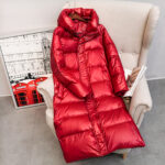 Doudoune fine mi-longue rouge chaude à col haut pour femme présentée à plat sur une chaise