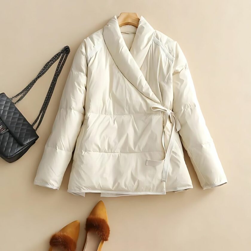 Doudoune courte portefeuille pour femme sur fond beige. On aperçoit un sac à main noir posé à côté.