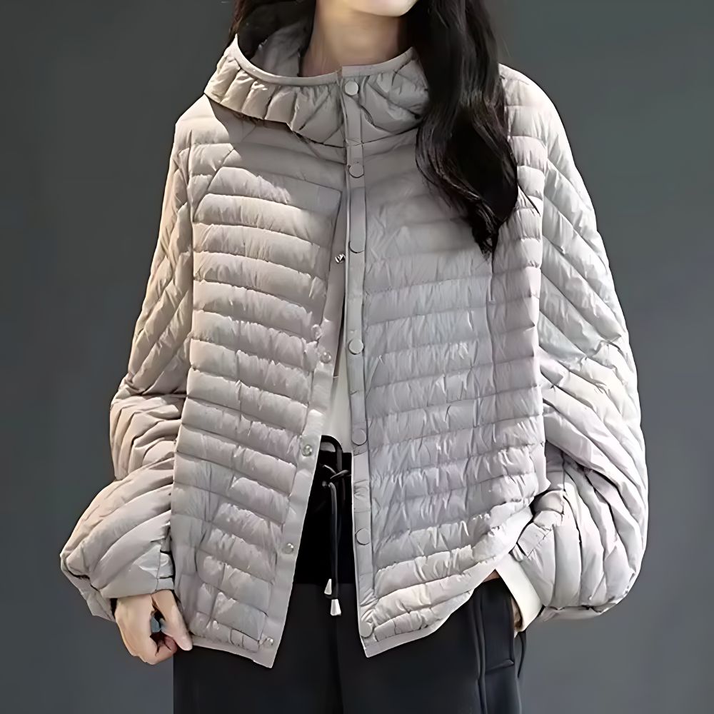 Une femme porte une doudoune tendance mode 2024 légère grise à capuche.