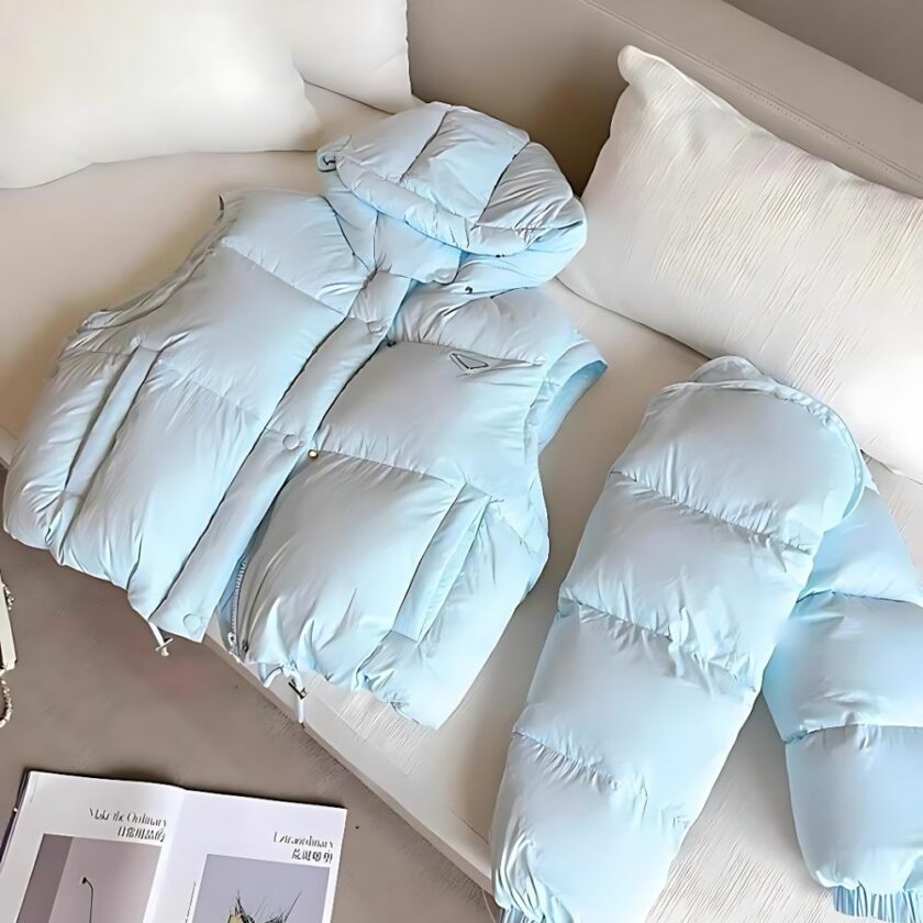 On a posé sur un canapé une doudoune bleu ciel sans manches et une autre doudoune avec manche cette fois pour montrer que le smanches sont amovibles sur cette doudoune à capuche