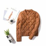 La doudoune façon bomber pour femme est posé un sol blanc avec un café, des documents et un cactus.